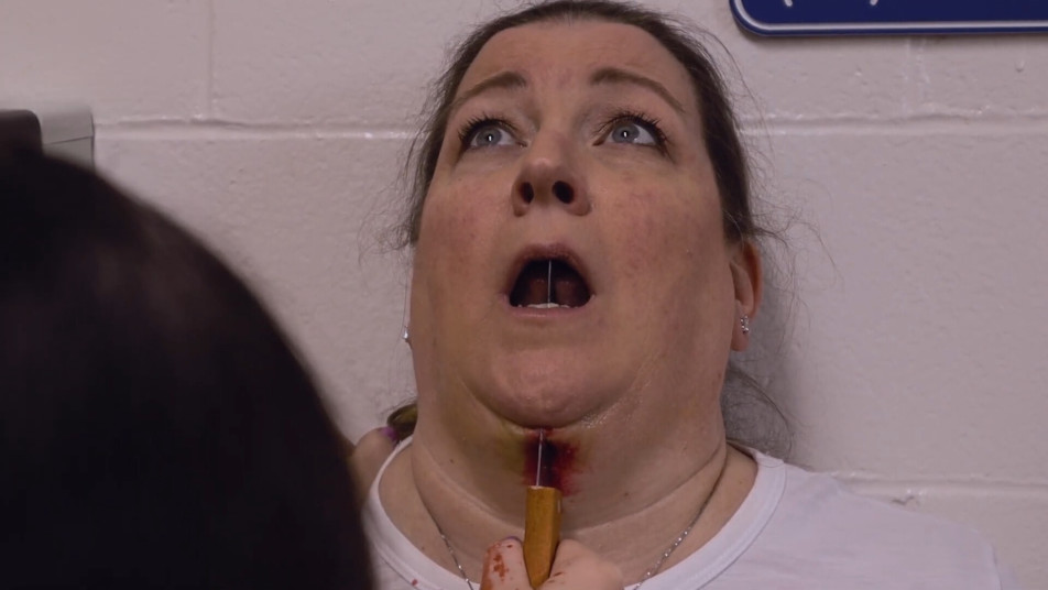 A woman with blood on her neck is being examined by a nurse at a high school.